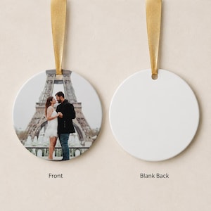 Puede incluir: Un adorno circular de cer&aacute;mica con una fotograf&iacute;a impresa de una pareja frente a la Torre Eiffel. El adorno tiene una cinta dorada para colgarlo. El reverso del adorno es de color blanco s&oacute;lido y est&aacute; en blanco.