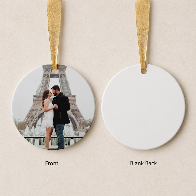 Puede incluir: Un adorno circular de cer&aacute;mica con una fotograf&iacute;a impresa de una pareja frente a la Torre Eiffel. El adorno tiene una cinta dorada para colgarlo. El reverso del adorno es de color blanco s&oacute;lido y est&aacute; en blanco.
