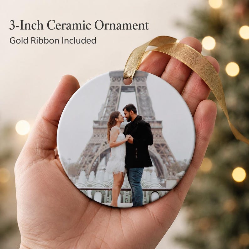 Puede incluir: Un adorno de cer&aacute;mica redondo de 7,62 cm con una fotograf&iacute;a impresa de una pareja frente a la Torre Eiffel. El adorno tiene un agujero en la parte superior con una cinta dorada para colgarlo. El texto 3-Inch Ceramic Ornament es visible.