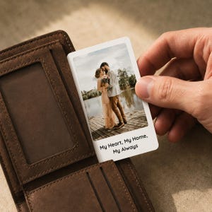May include: A brown leather wallet with a clear ID window. A small white card with a photo of a couple kissing is being held up. The card has the text "My Heart, My Home, My Always".