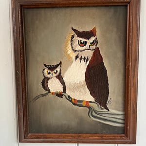 May include: Vintage framed painting of two owls perched on a branch. The larger owl has brown and white feathers with a stern expression. The smaller owl is brown and white. The artwork is signed and dated '79.
