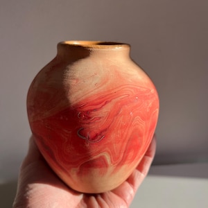 May include: A small, hand-painted ceramic vase with a marbled design in shades of orange and red.