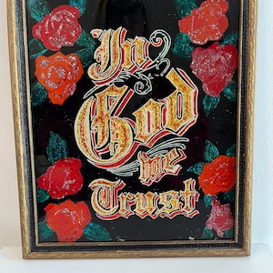 May include: Framed artwork with a black background featuring the words "In God We Trust" in gold lettering with red and green accents. The artwork is surrounded by red roses with glitter accents.