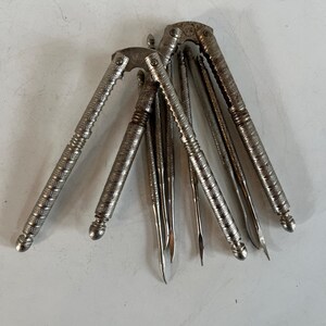May include: A collection of vintage silver-toned nutcrackers and picks. The nutcrackers have textured handles and the picks are slender with pointed ends. The items are arranged on a light-colored surface, suggesting a kitchen or dining setting.