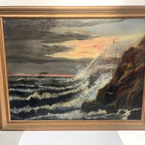 May include: A framed oil painting depicting a seascape with a rocky cliff, crashing waves, and a ship in the distance. The sky is a mix of dark clouds and a vibrant orange sunset.