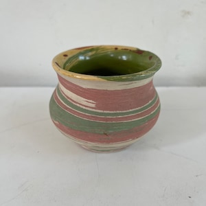 May include: A small, green, pink, and white ceramic vase with a rounded bottom and a wide opening.