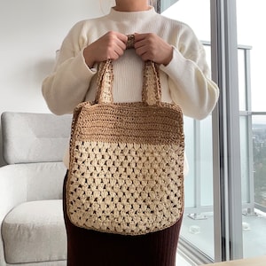 May include: A brown and cream crocheted tote bag with a wide, flat base and two handles. The bag is made of a thick, textured yarn and has a simple, classic design.