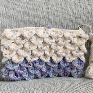 Peut inclure: Un sac à main en crochet avec un design ombré blanc et violet. Le sac à main a une petite poignée et une bandoulière détachable.