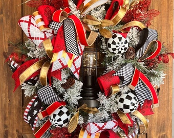 May include: A Christmas wreath with red, white, and black checkered ribbon, gold ribbon, and red and white striped ribbon. The wreath is decorated with gold leaves, pine cones, and black and white ornaments. A black lantern with a light bulb is in the center of the wreath.