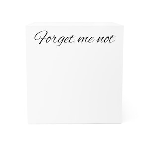 May include: A white, square block with the cursive text "Forget me not" in black. The block has a clean, minimalist design.