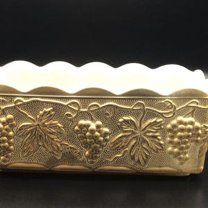 May include: A gold-colored rectangular planter with a scalloped rim and embossed grapevine design.
