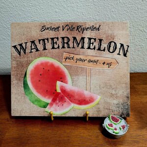 Pode incluir: Uma placa de madeira r&uacute;stica com o texto "Sweet Vine Ripened Watermelon - pick your own - 4 mi" e uma ilustra&ccedil;&atilde;o em aquarela de fatias de melancia.