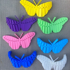 May include: Seven colorful butterfly-shaped ornaments made of plastic. The butterflies are in various colors, including yellow, purple, green, pink, blue, and white.