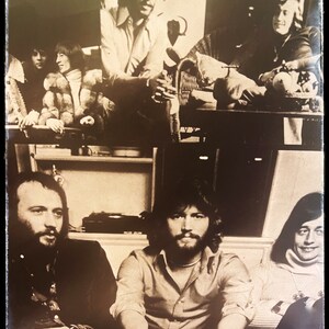 May include: A black and white photo of a group of people. The photo is taken from the waist up and shows the people smiling and looking at the camera. The people are wearing casual clothing. The photo is taken in a room with a wooden floor and a white wall.