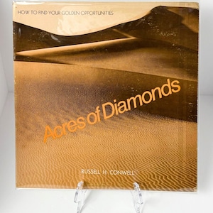 May include: A book cover with a desert landscape in shades of brown and tan. The title "Acres of Diamonds" is in orange, with the author's name at the bottom. The top reads "How to Find Your Golden Opportunities".