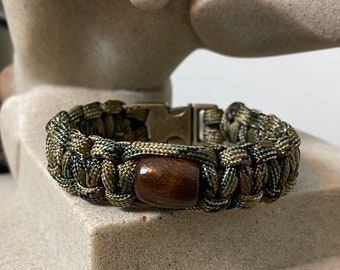 Pulsera de supervivencia artesanal de paracord 550 con cuentas de madera y hebilla metálica.
