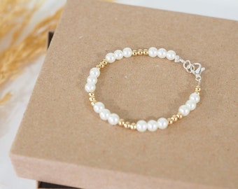 May include: A delicate bracelet made with white faux pearls and gold beads. The bracelet has a silver clasp.