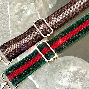 May include: Two adjustable bag straps featuring sparkling rhinestone embellishments. One strap is brown with a central light-colored stripe, and the other is green with a central red stripe. Both include gold-tone metal hardware and lobster clasps.