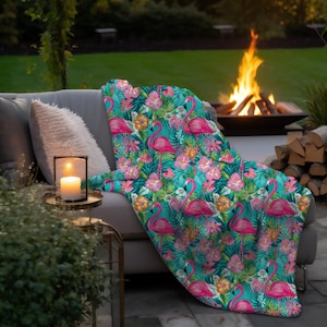 May include: A teal blue throw blanket with a tropical print featuring pink flamingos, green palm leaves, and pink flowers. The blanket is draped over a gray couch.