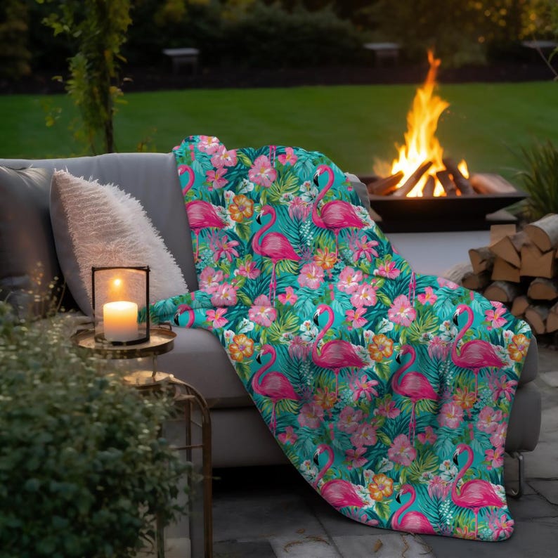 May include: A teal blue throw blanket with a tropical print featuring pink flamingos, green palm leaves, and pink flowers. The blanket is draped over a gray couch.