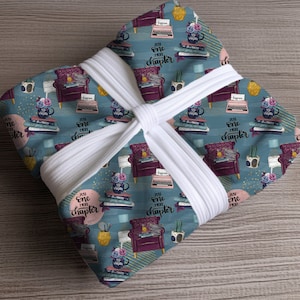 May include: A blue and pink patterned gift wrap with a repeating design of a typewriter, a stack of books, a chair, and the text "Just one more chapter".