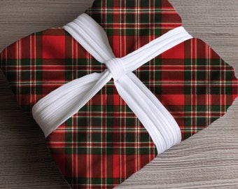May include: A wrapped gift with a red, green, and white plaid pattern. The gift is tied with a white ribbon, creating a festive and classic presentation. The plaid design is a traditional holiday pattern.