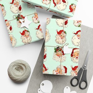 May include: A set of three vintage-style Christmas wrapping paper sheets with a repeating pattern of Santa Claus faces on a light green background. The paper is decorated with white snowflakes and red holly.