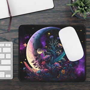 Puede incluir: Una alfombrilla de ratón negra con un diseño de luna creciente. La luna está llena de flores y estrellas moradas, rosas y azules. La alfombrilla de ratón es perfecta para añadir un toque de fantasía a tu espacio de trabajo.