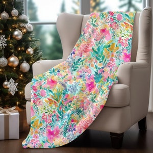 May include: A soft, floral throw blanket with a watercolor design featuring pink, yellow, and blue flowers on a white background.