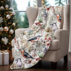 Op de afbeelding: Een zachte, witte deken met een aquarelontwerp van vogels en bloemen. De vogels zijn blauw, groen en bruin, en de bloemen zijn rood en roze.