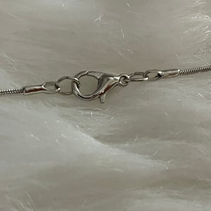 May include: Close-up of a silver chain necklace clasp with a lobster claw closure.