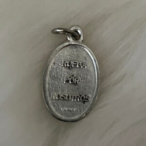 May include: Silver oval charm with the words "Ruega por nosotros" engraved on it.