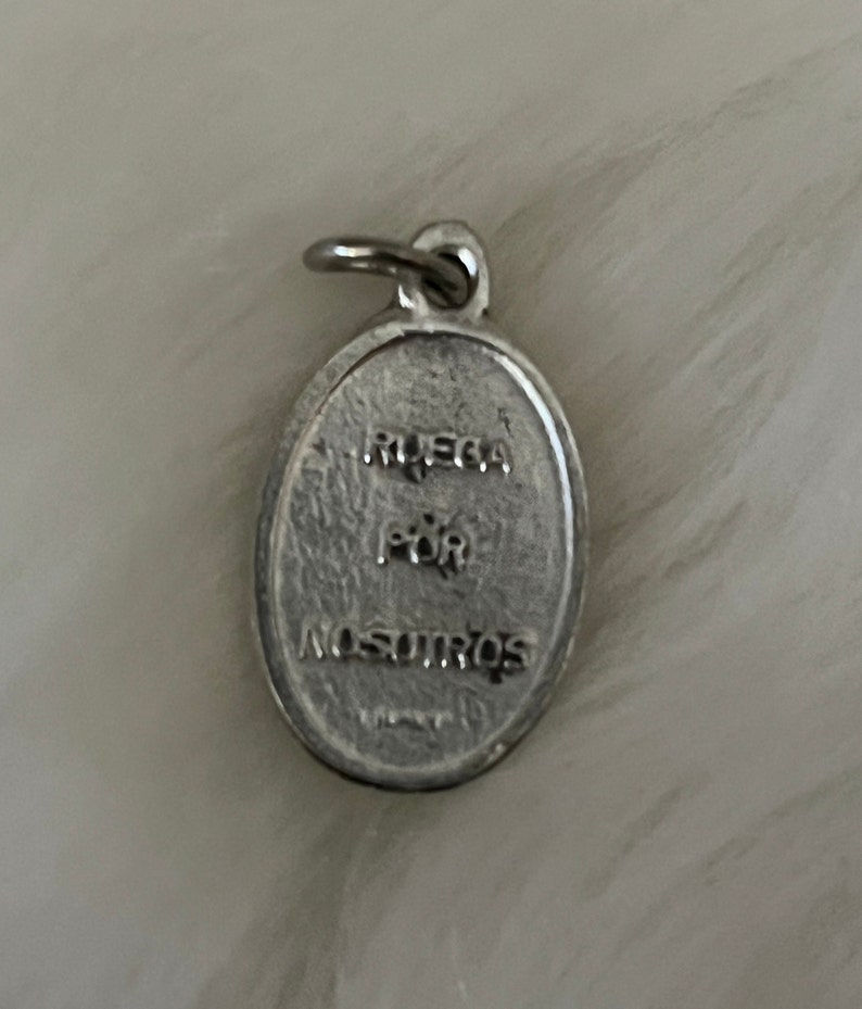 May include: Silver oval charm with the words "Ruega por nosotros" engraved on it.