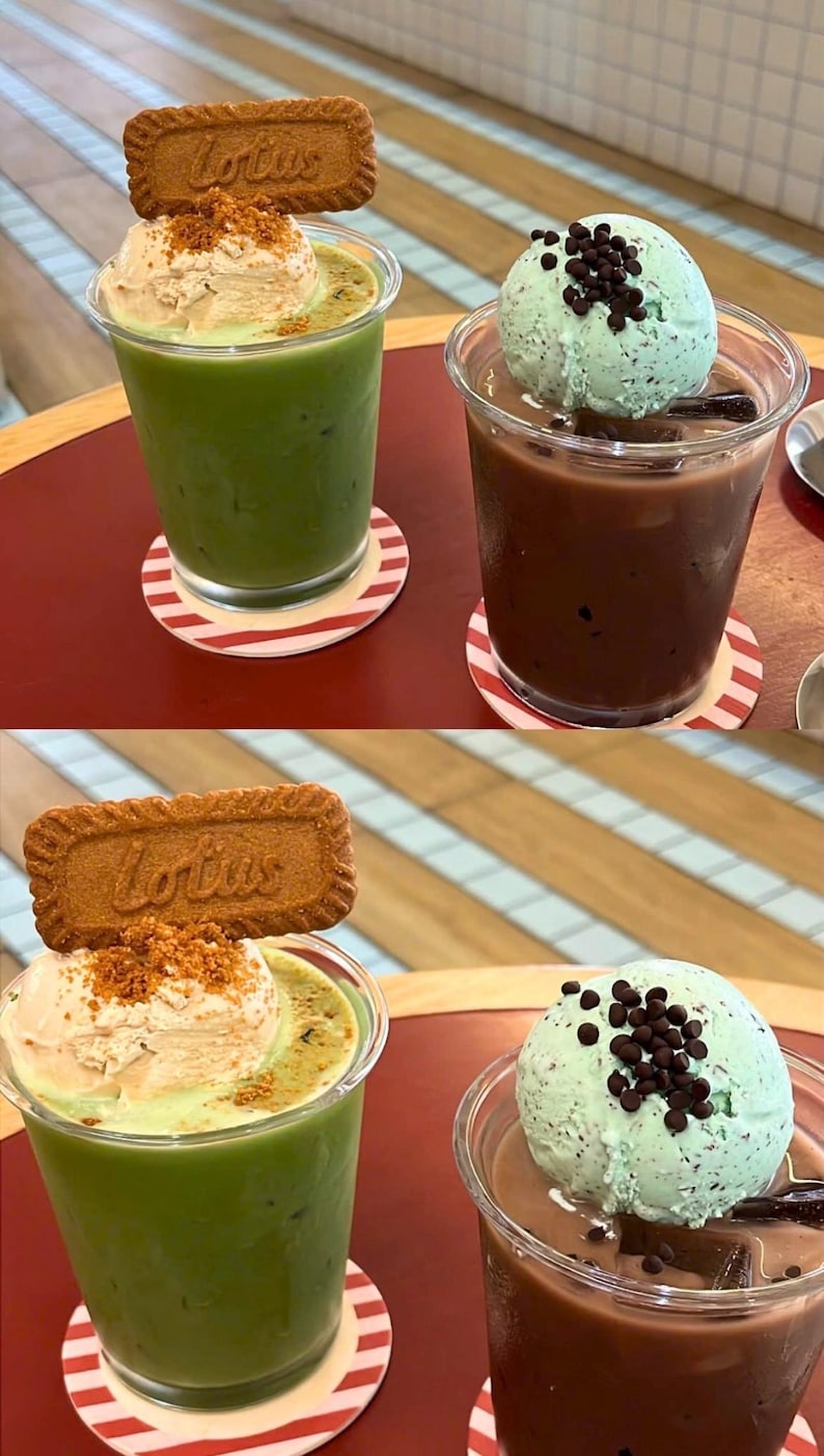 May include: Two clear plastic cups with drinks and toppings. One has a green drink with ice cream and a cookie. The other has a brown drink with mint ice cream and chocolate chips. Both are on red and white striped coasters.