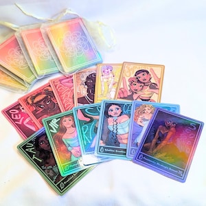 Könnte beinhalten: Eine Sammlung von Tarotkarten mit farbenfrohen Illustrationen und holografischen Akzenten. Die Karten zeigen Tierkreiszeichen und Sätze wie "Intuitive Creative" und "Passionate Strategic Moment". Einige Karten befinden sich in schillernden Beuteln.