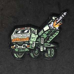 Puede incluir: Parche bordado verde de un camión militar con un misil lanzándose desde la parte trasera. El camión tiene las palabras "Libertad de la opresión" escritas en la parte delantera.