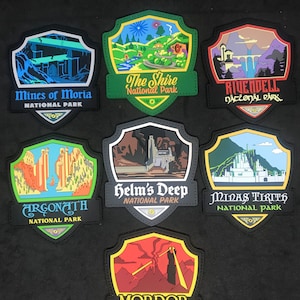 Pode incluir: Sete patches coloridos em forma de escudo com imagens e texto de O Senhor dos Anéis. Os patches são etiquetados como "Minas de Moria Parque Nacional", "A Shire Parque Nacional", "Rivendell Parque Nacional", "Argonath Parque Nacional", "Helm's Deep Parque Nacional", "Minas Tirith Parque Nacional" e "Mordor Parque Nacional".
