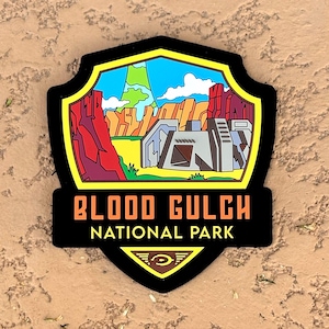 May include: A black and yellow shield-shaped patch with a cartoon image of a landscape with a building and a mountain in the background. The text "BLOOD GULCH NATIONAL PARK" is printed in orange and black letters on the patch.