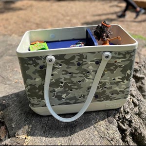 May include: A white and gray camo tote bag with white handles and a blue interior. The bag has a removable divider and a logo that says "b.o.b.b.e".