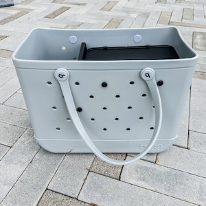 May include: A light gray tote bag with black handles and a black removable insert. The bag has a white logo that says "b.gg" and a pattern of small holes.