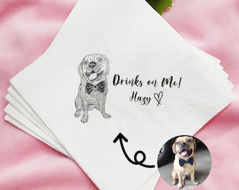 May include: White paper napkins with a black and white illustration of a dog wearing a bow tie. The text "Drinks on Me! Hazy ♡" is printed on the napkin.
