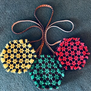 May include: Three crocheted purses with floral designs. The purses are yellow, red, and green. Each purse has a brown leather strap.