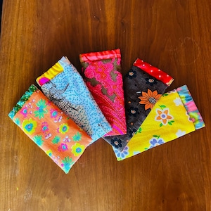 May include: Five colorful fabric eyeglass cases with different patterns. The cases are made of a soft, textured fabric and have a variety of floral, geometric, and abstract designs.