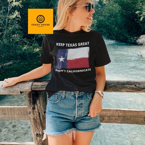 May include: A black t-shirt with the text "Keep Texas Great" and a stylised image of the Texas flag. The text "Don't Californicate" is below the flag. The t-shirt is being worn by a person standing on a wooden bridge.