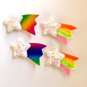 May include: Four white star-shaped embellishments with rainbow-colored felt tails. The stars are made of iridescent sequins.