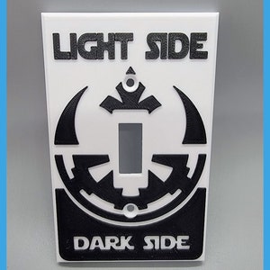 May include: White light switch cover with a black Star Wars themed design. The top of the cover says "LIGHT SIDE" and the bottom says "DARK SIDE".