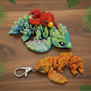 May include: Three colourful, 3D-printed dragon figurines. One is a keychain with a silver clasp, and the other two are larger, with red, green, blue, and yellow hues. The dragons have detailed scales and bird-like features.