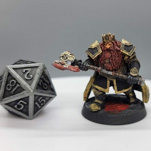 May include: A silver metal 20-sided die with black numbers, and a miniature painted figurine of a dwarf king wearing a black and gold armor, holding a warhammer.