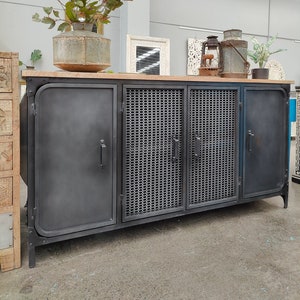 May include: A dark grey metal cabinet with a light wood top. The cabinet has four doors, the centre two with a mesh design. Decorative items, including a vase with greenery, sit on top. The cabinet is approximately 152 cm long.