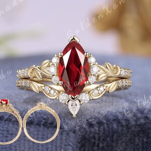 May include: A set of gold rings featuring a marquise-cut red gemstone as the centerpiece, surrounded by smaller white gemstones. The rings have a floral design and the text "GOLDENXANADU" is at the top.